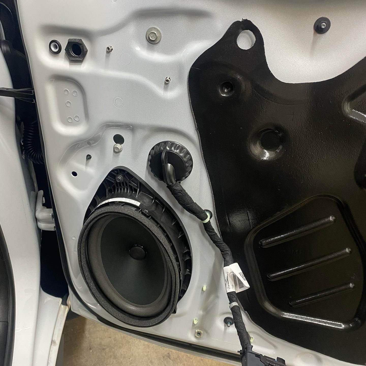 Interior car door frame with a speaker installed, wires, and sound dampening material. White, black, and gray colors are visible.