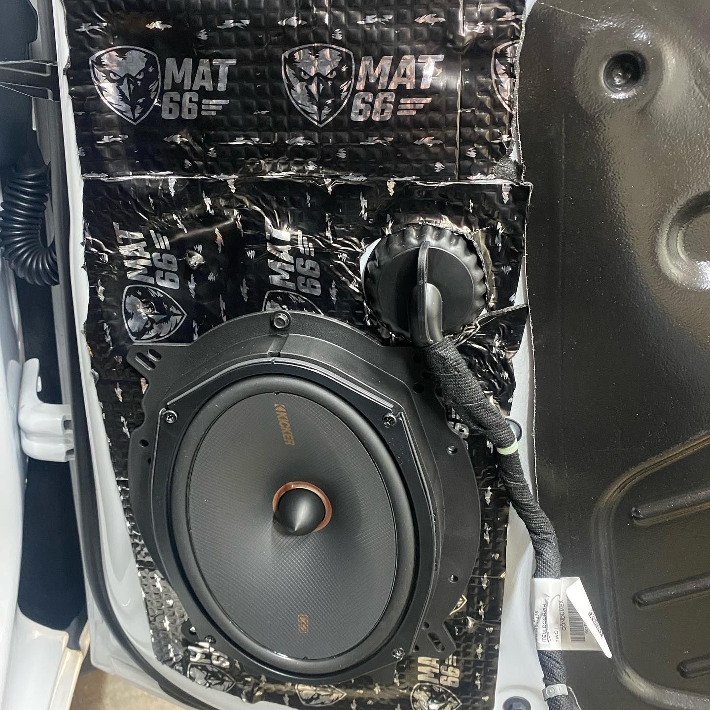 A car door with sound dampening material and a large speaker installed, with black and white details.