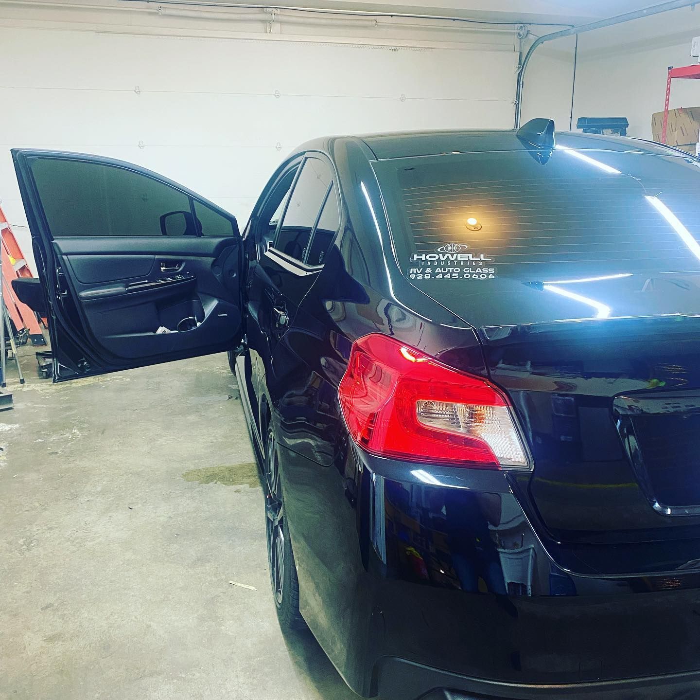Black sedan with tinted windows and open driver's side door parked inside a well-lit garage.