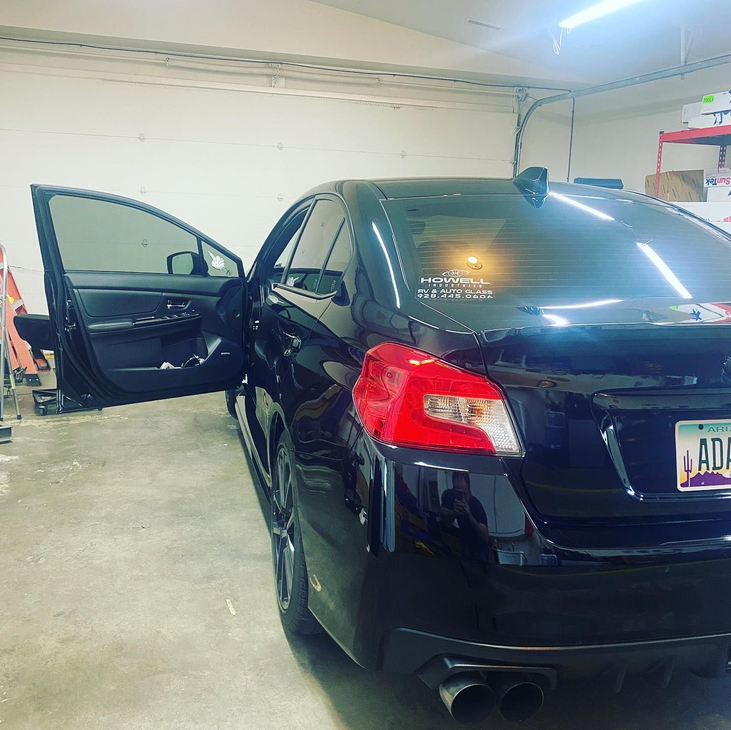 Black Subaru sedan with tinted windows parked indoors, door open.