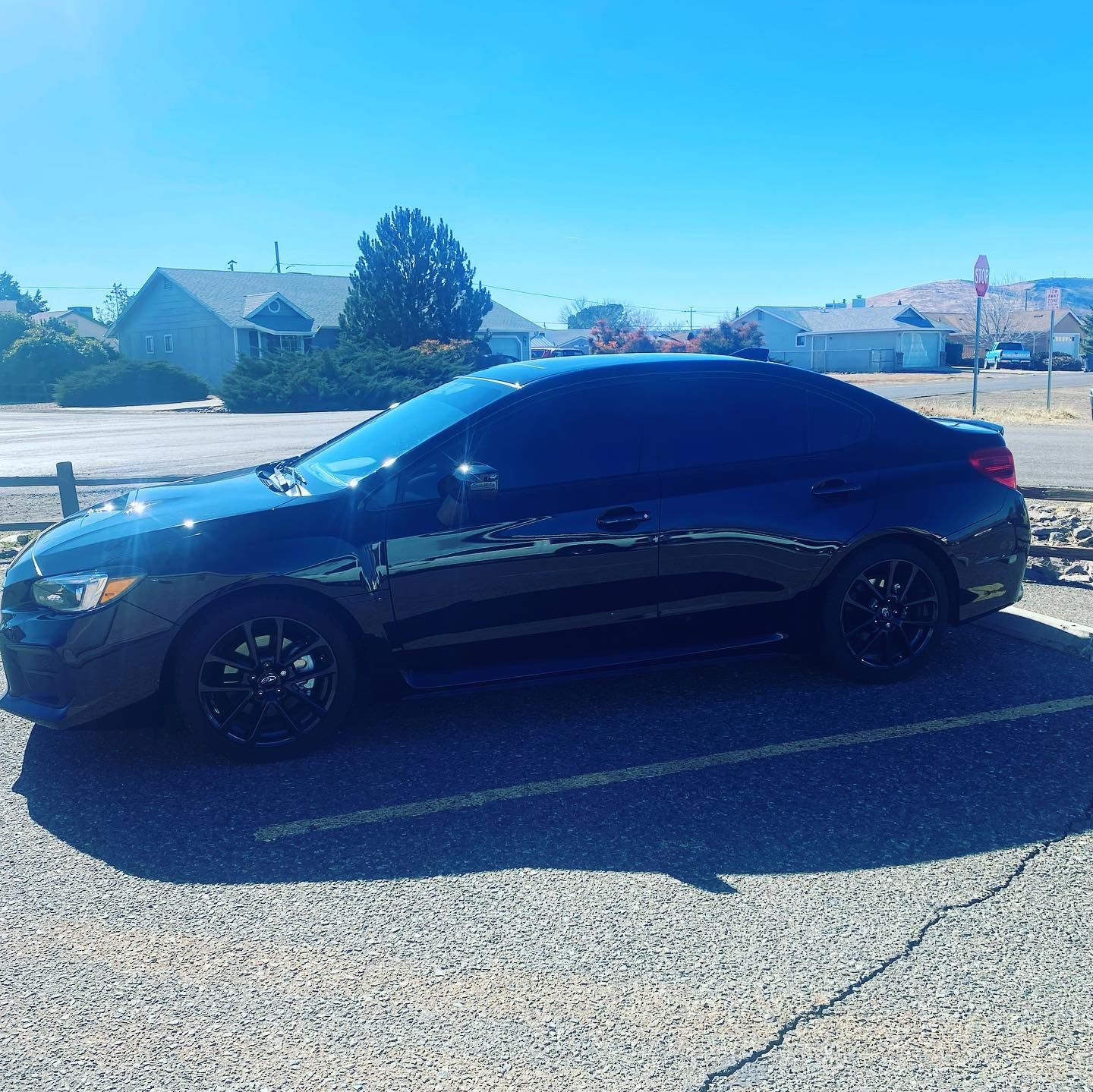 Black Subaru sedan parked in a lot on a sunny day, with dark tinted windows and black rims.