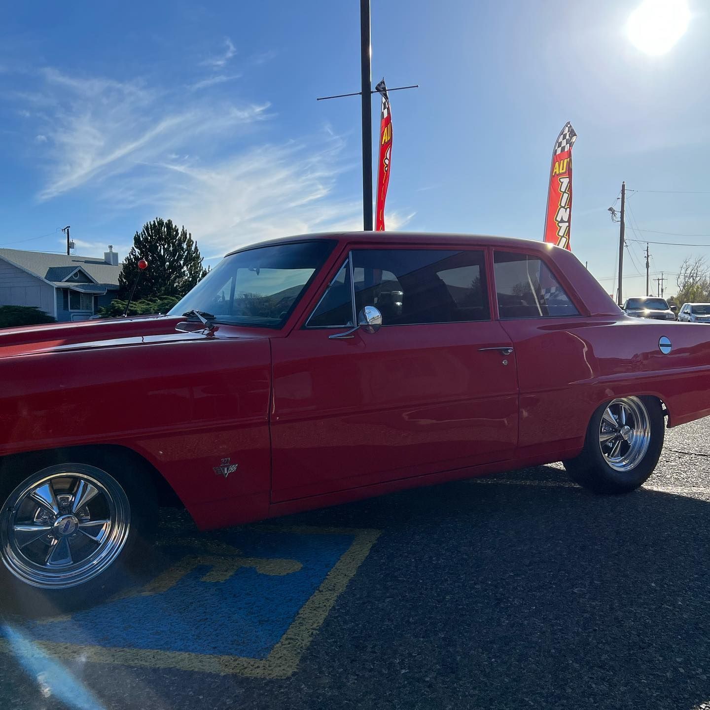 Red classic car parked in a parking space on a sunny day. Chrome wheels and a blue sky are visible.