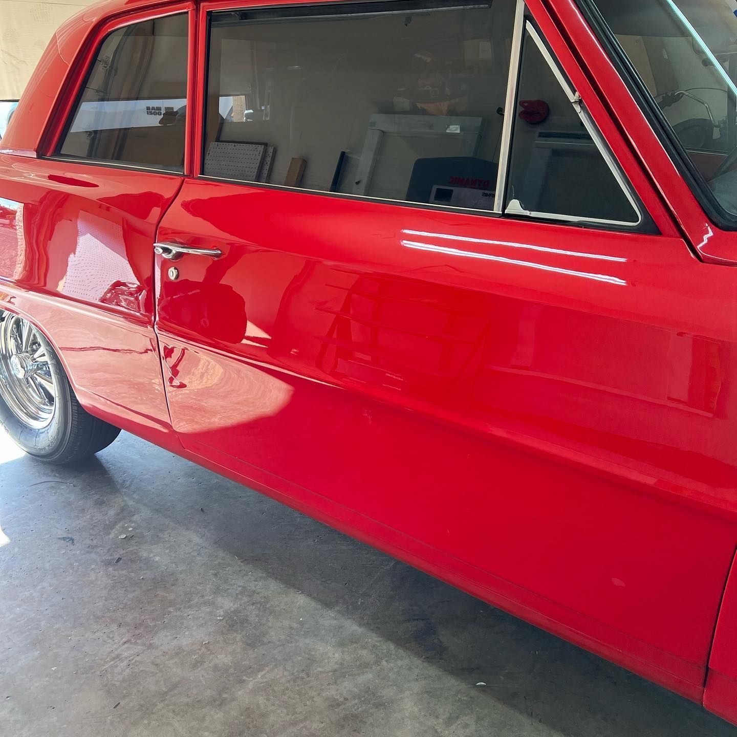 A shiny red classic car, likely a Chevrolet Nova, parked inside with reflections in the windows.