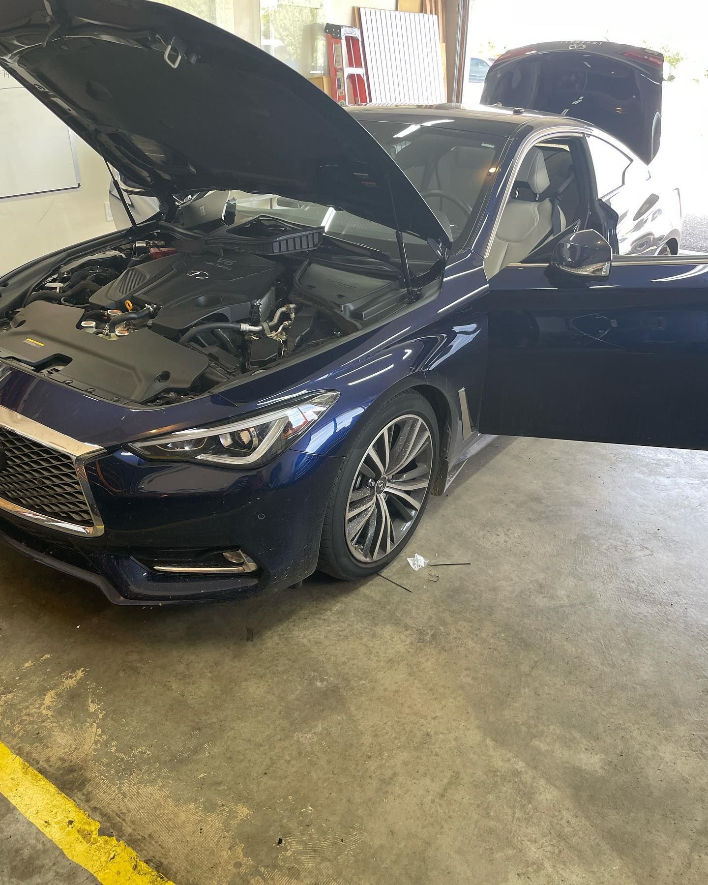 Blue Infiniti coupe with hood, trunk, and door open, in a garage.