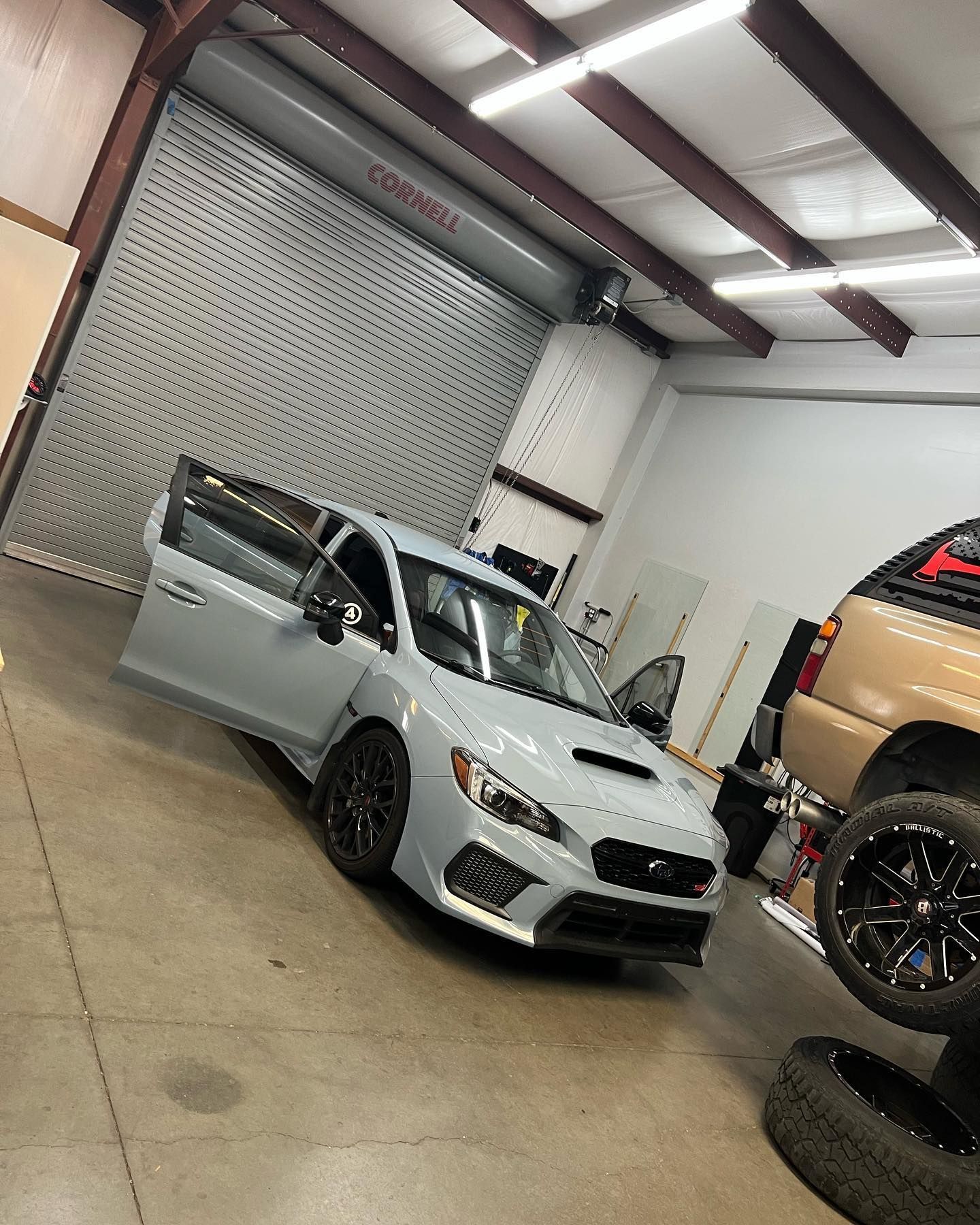 A gray Subaru WRX with open doors inside a garage, a closed garage door in the background.