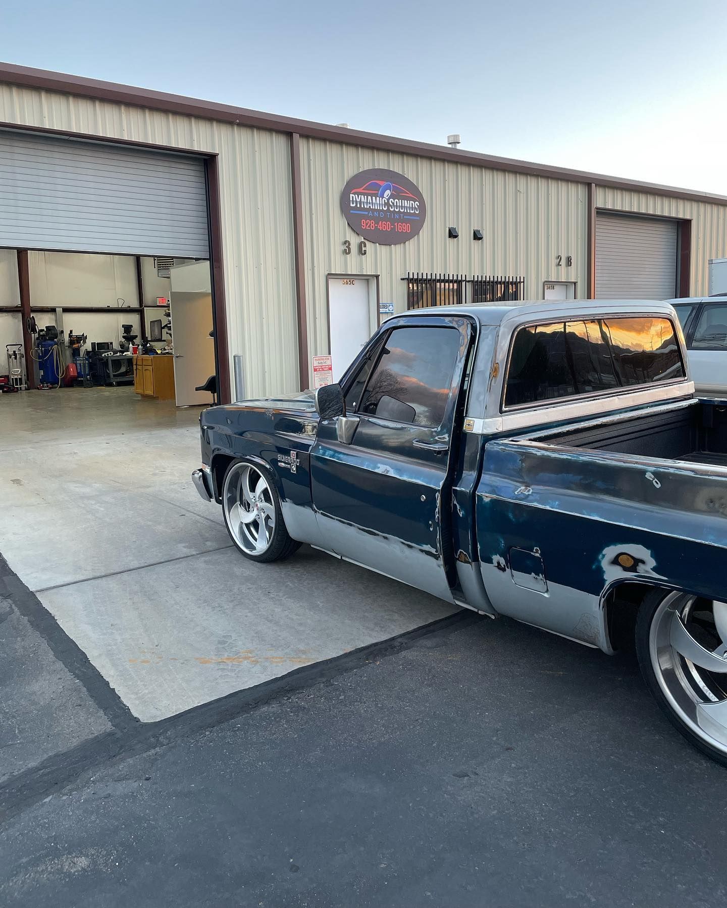 Blue and silver pickup truck parked outside a garage with the logo 