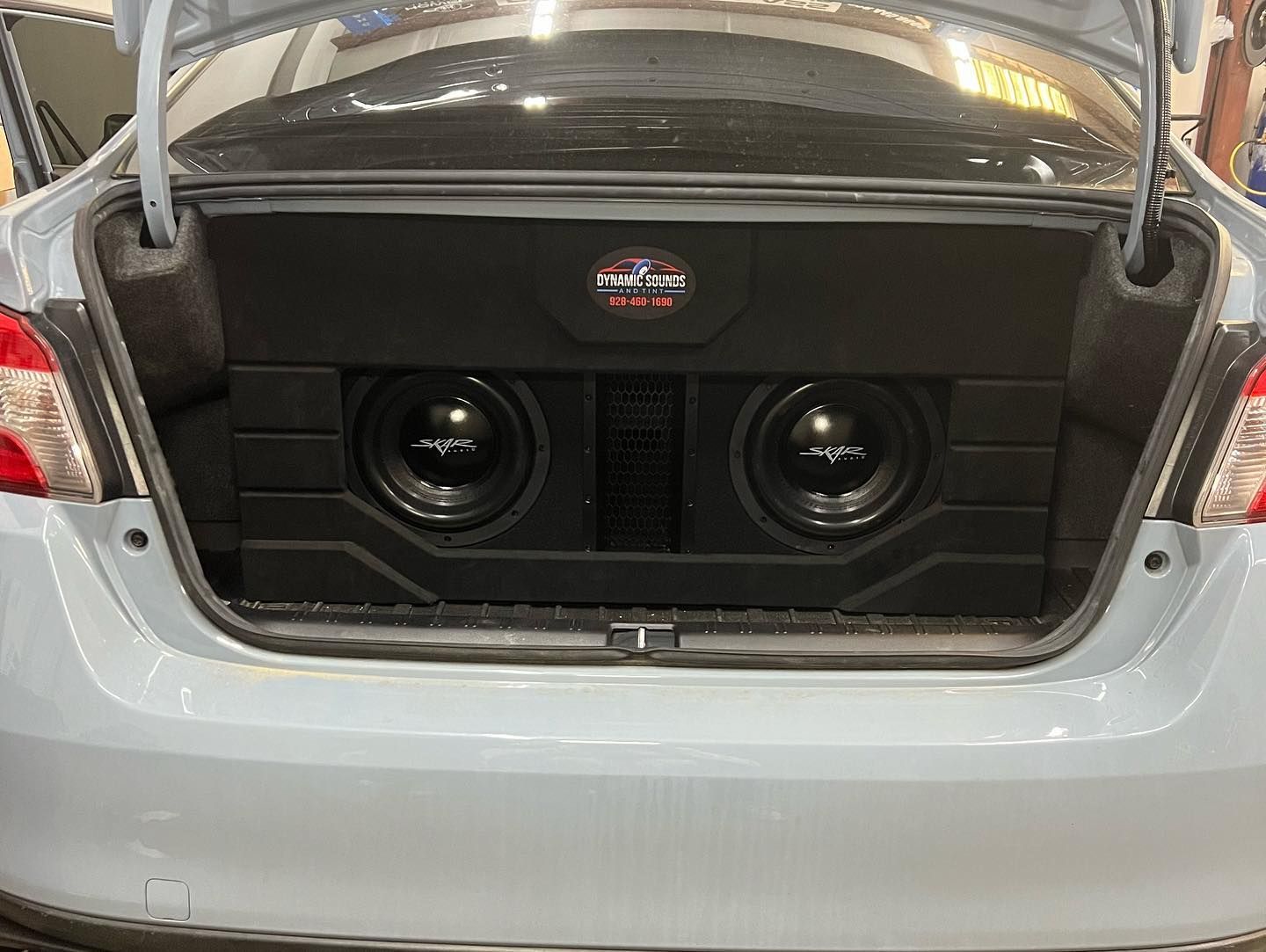 A car trunk with a custom subwoofer enclosure. Two black subwoofers are mounted within the box, which is black and gray.