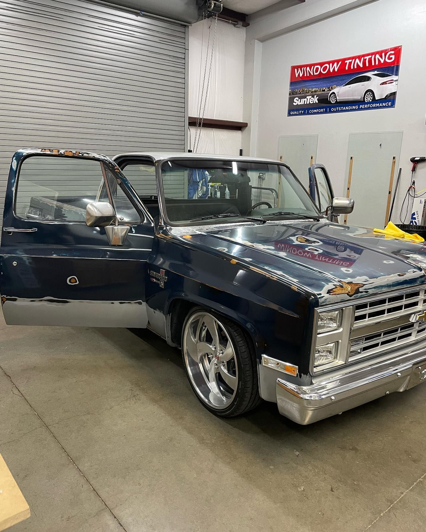 Dark blue classic pickup truck with chrome accents parked inside a window tinting shop, doors open.