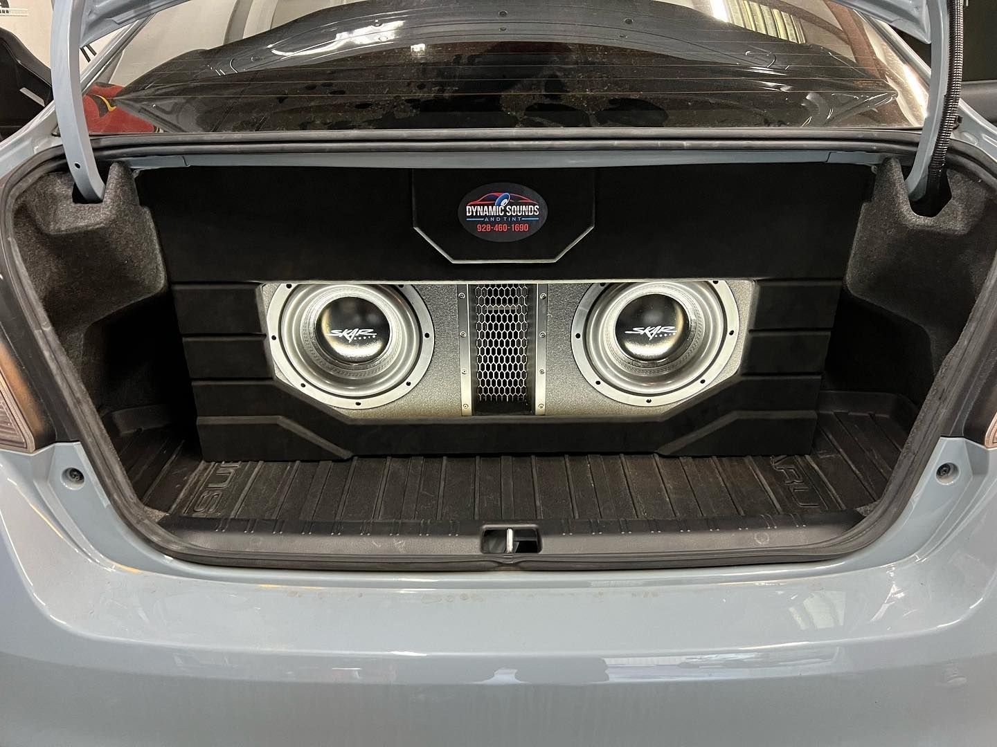 A car trunk displaying a custom audio system with two large speakers and a central amplifier, all encased in black and silver.