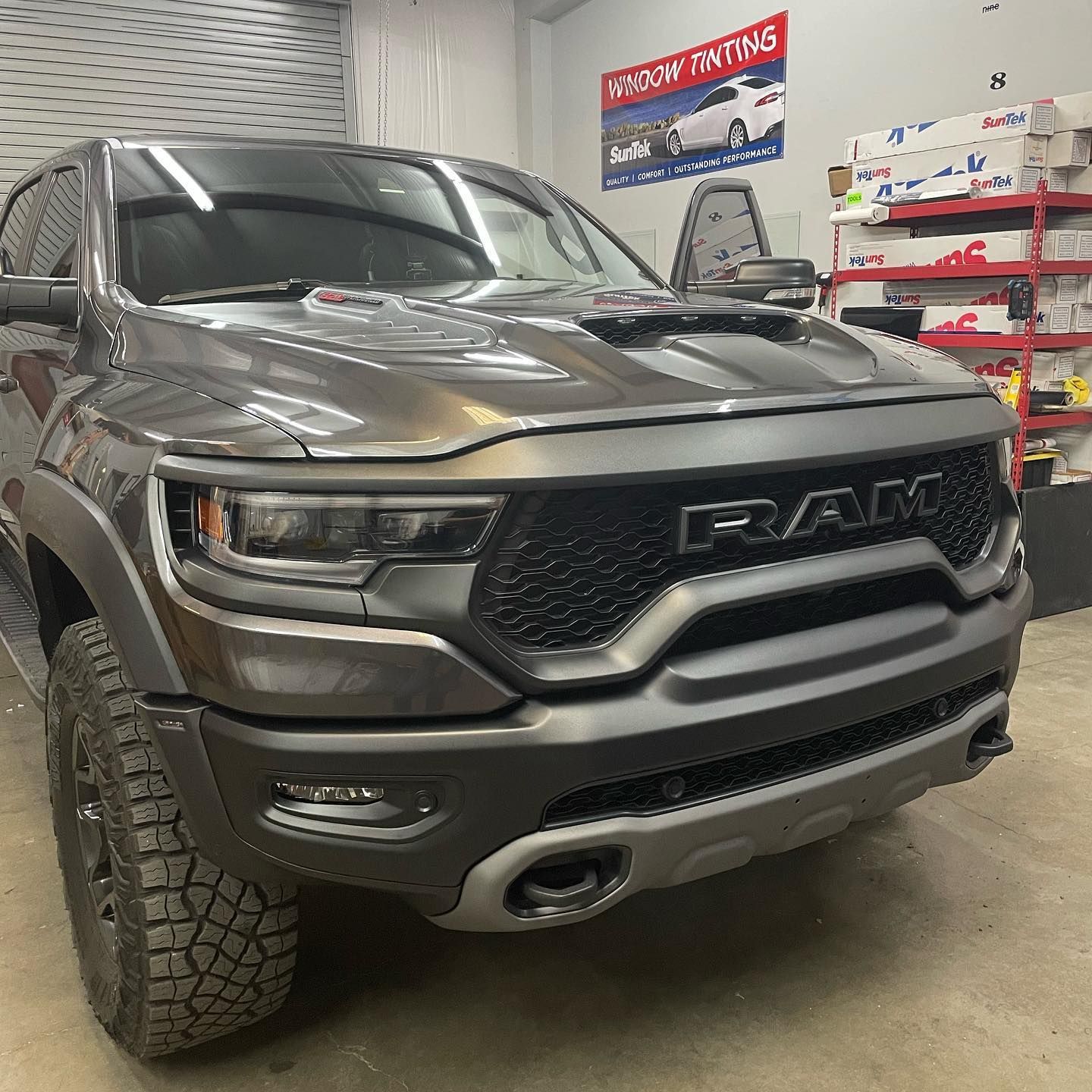 Dark gray Ram TRX truck parked inside a shop. The front of the truck is in focus, with black grille and off-road tires.