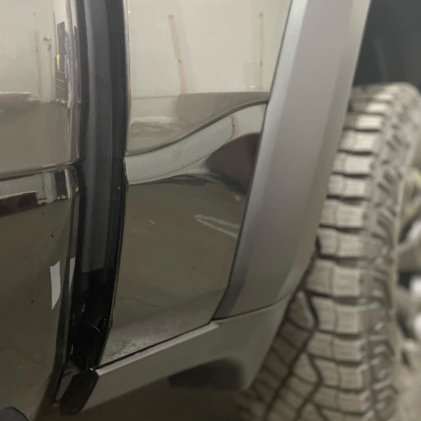 Close-up of a gray truck's rear door, showing the door's edge, black seal, and part of a large tire.