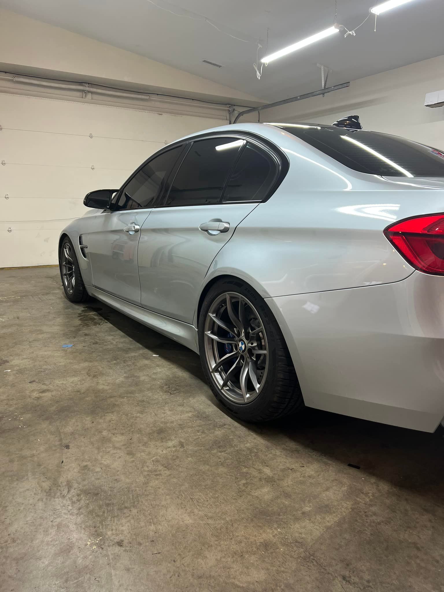 A silver BMW sedan with tinted windows parked in a garage. The car has custom wheels and a lowered stance.
