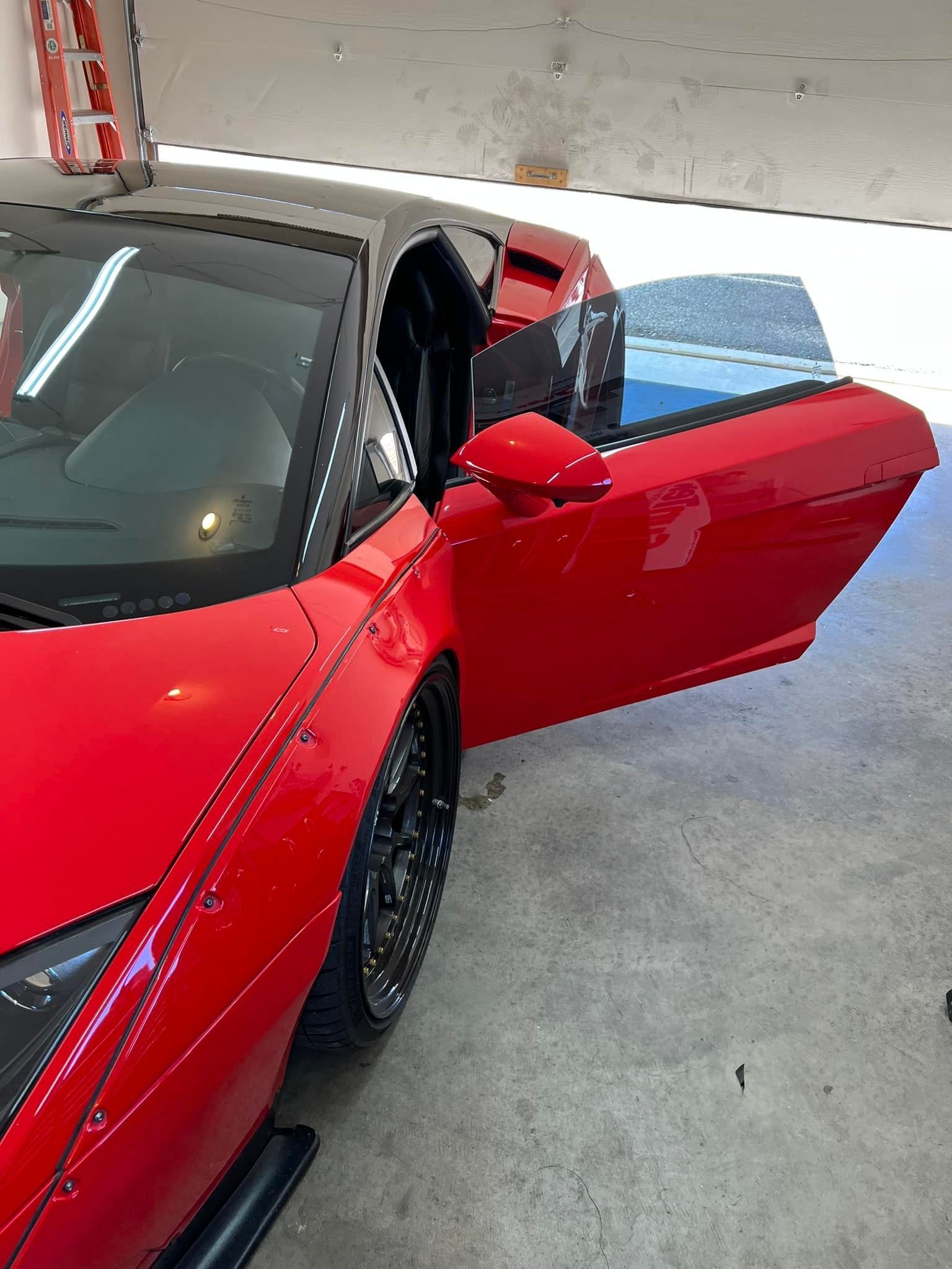 Red sports car with open door. A black sports car is in the background.