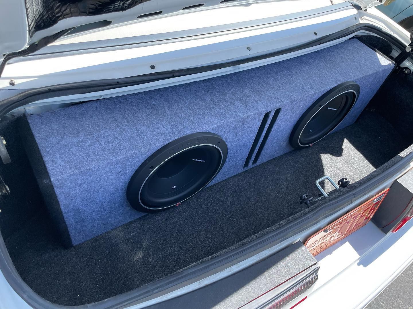 A white car trunk with a blue carpeted subwoofer box containing two speakers.