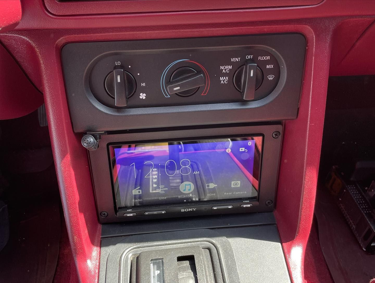 Dashboard of a red Ford Mustang with aftermarket car stereo and air conditioning controls.
