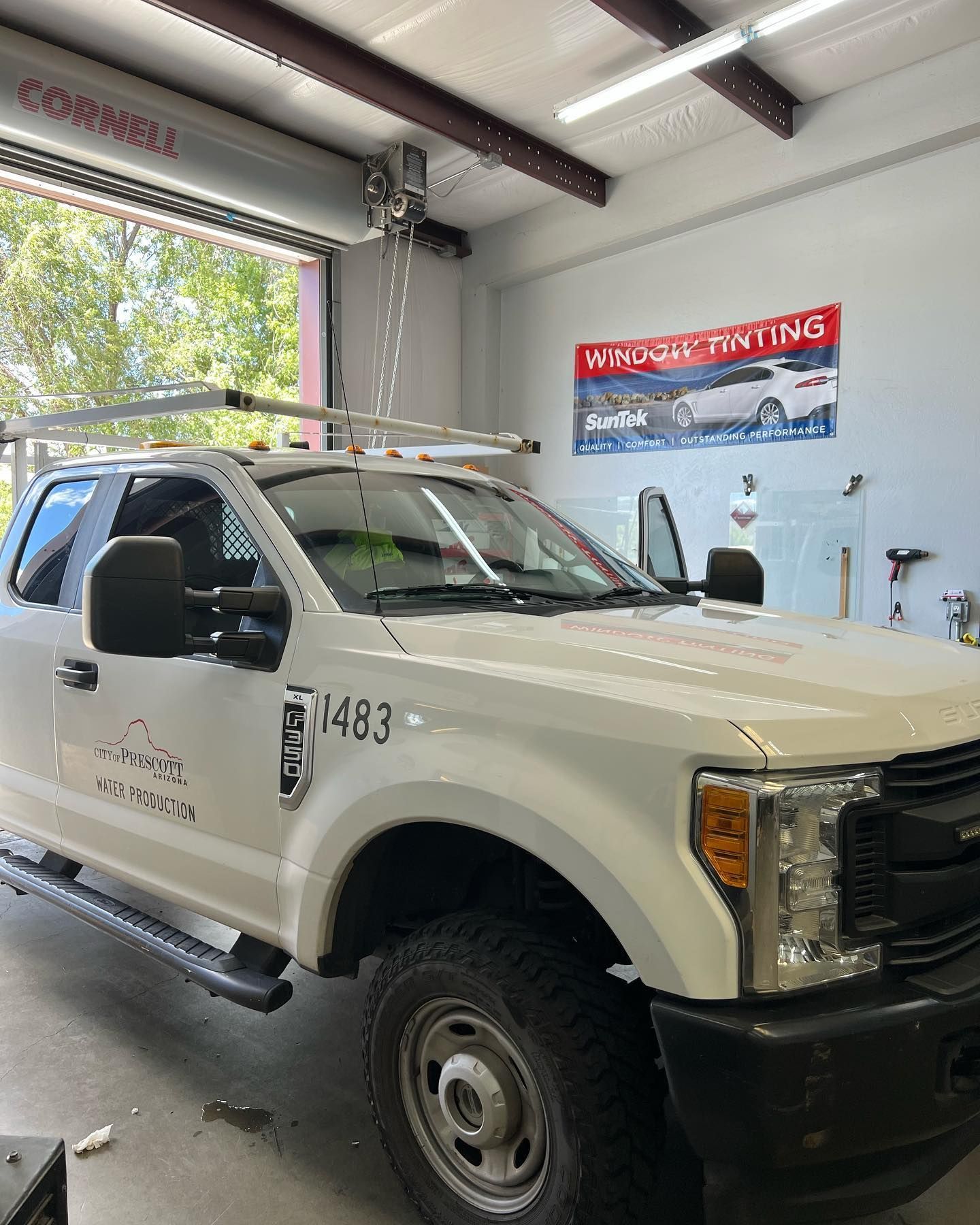 White truck with a ladder rack parked inside a garage. The door is open, and tinted glass is visible in the background.
