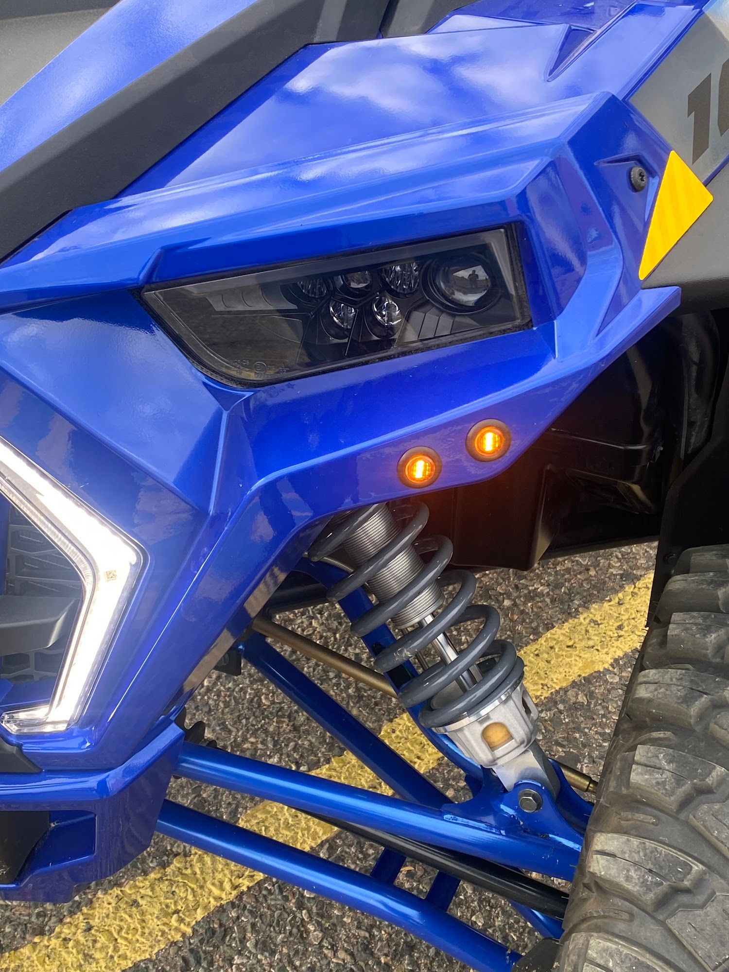 Blue off-road vehicle front quarter with a black headlight and orange lights, with a shock absorber visible.