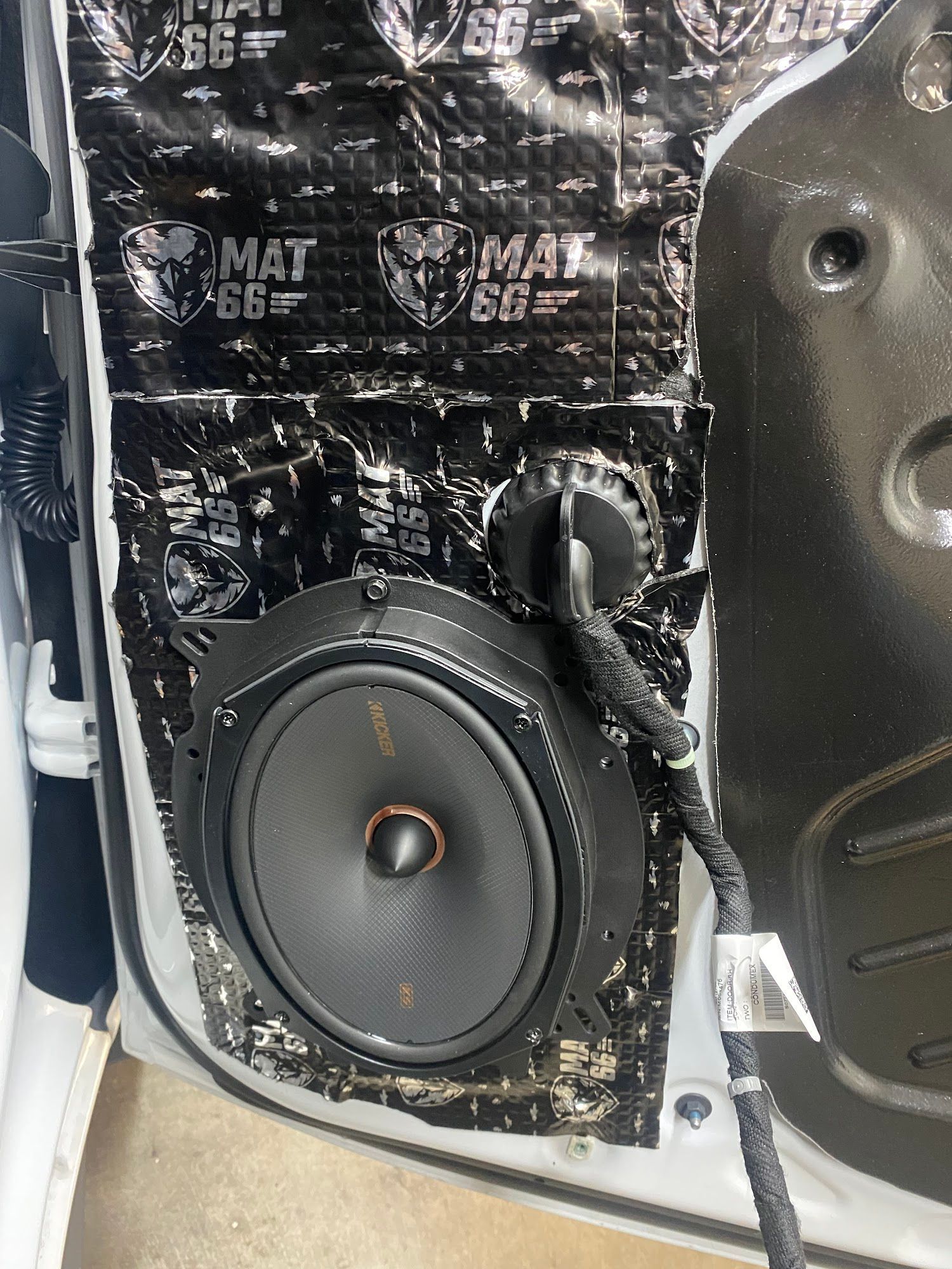 A car door panel with sound-dampening material installed. A large, black speaker is visible.