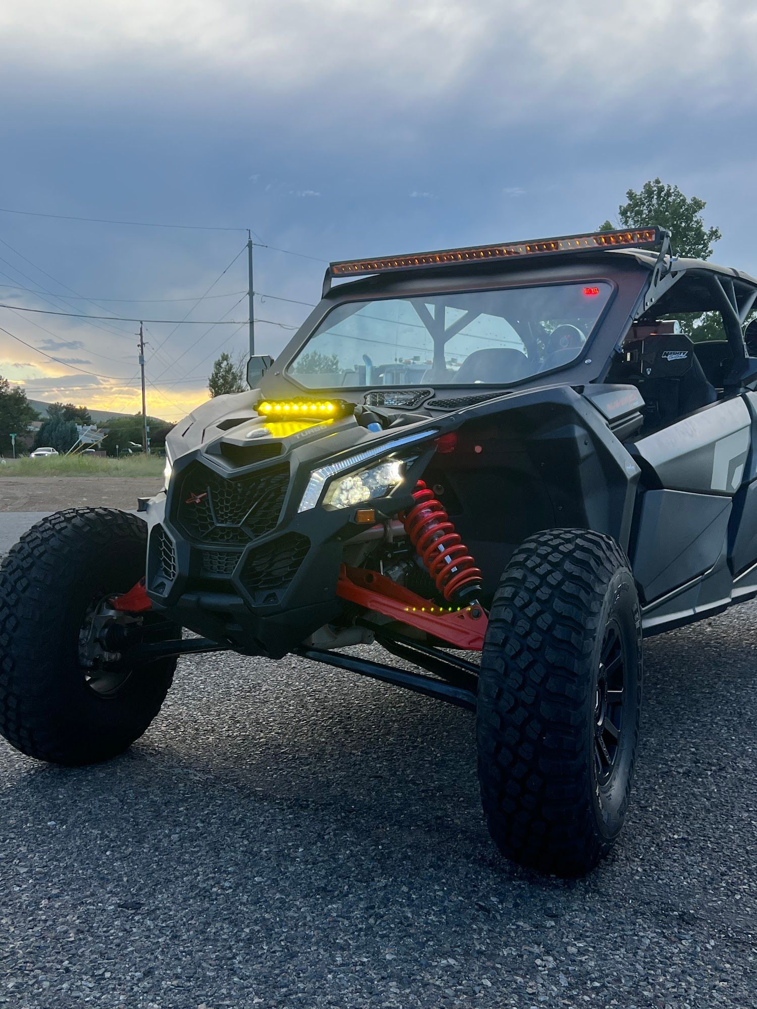 Black and silver Can-Am Maverick X3 side-by-side with off-road tires and LED light bars, parked on pavement.