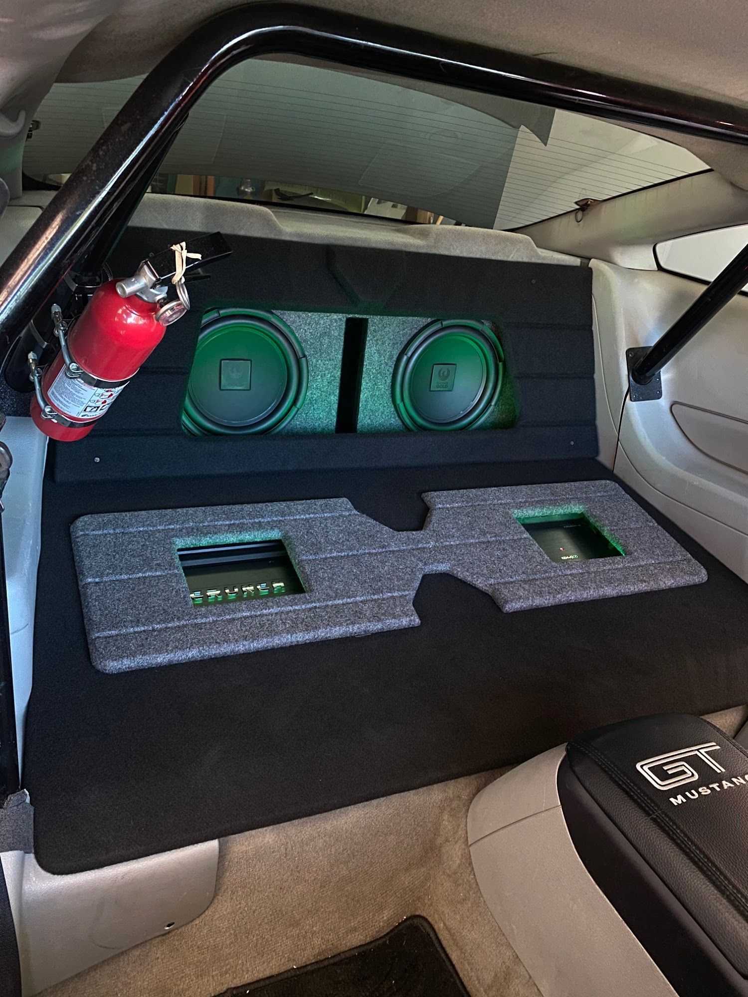 Custom car audio system with black and green speaker boxes, a fire extinguisher, and a roll cage in a car.