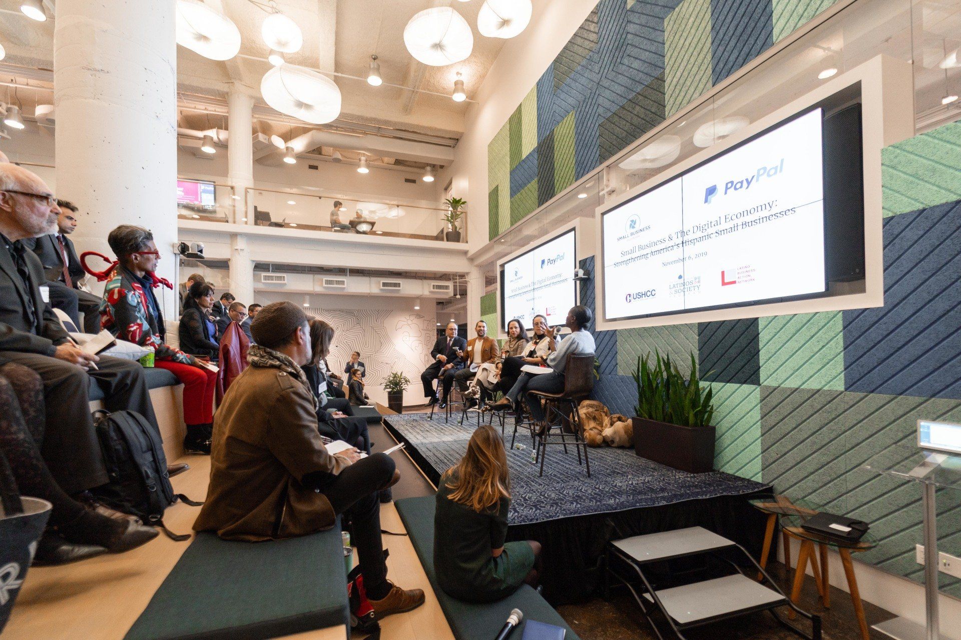 A group of people are sitting in a room watching a presentation on a stage.