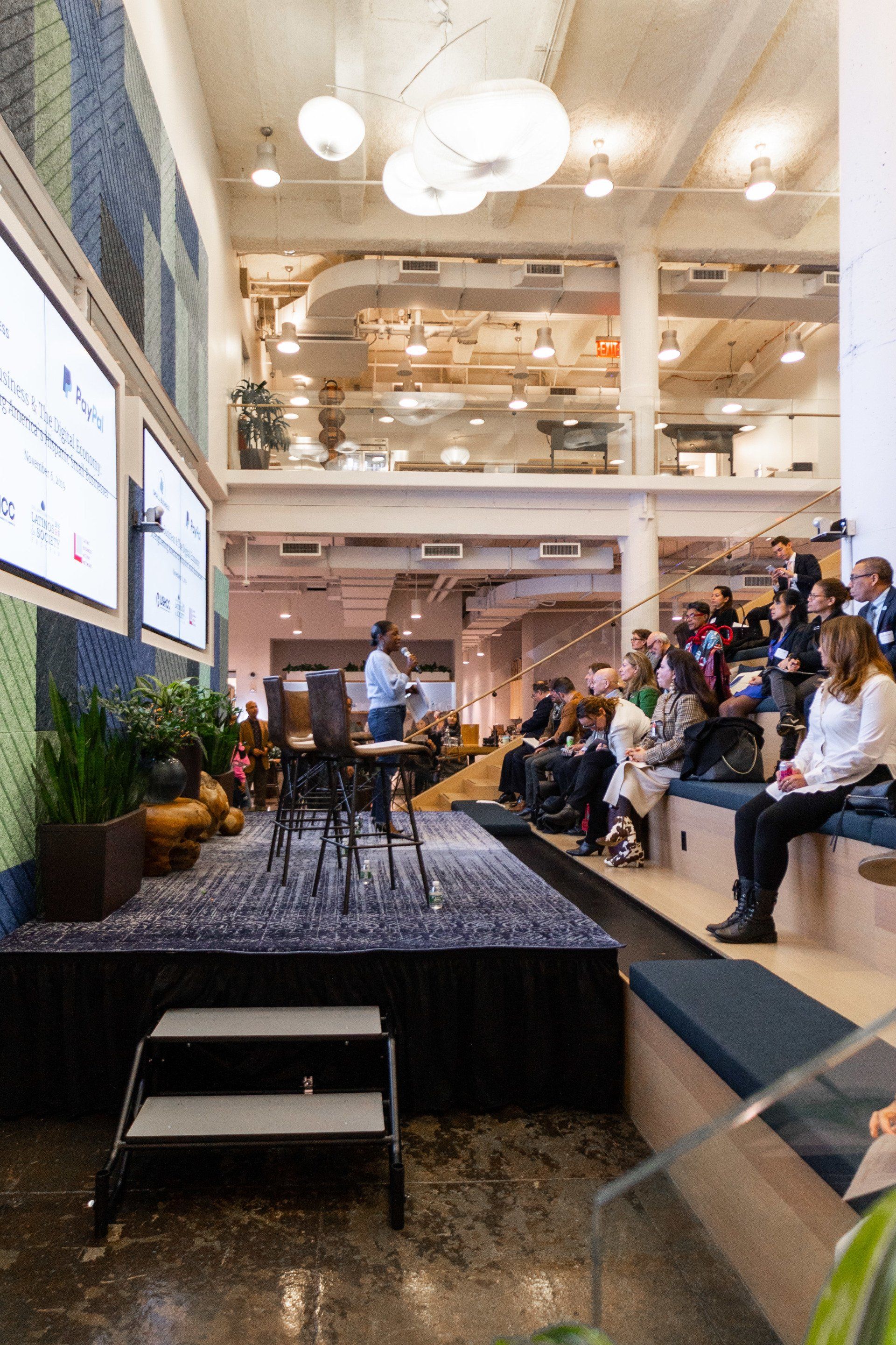 A group of people are sitting on steps in front of a stage in a large room.
