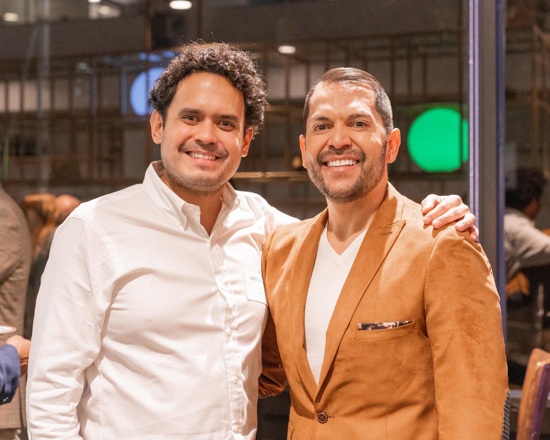 Two men are posing for a picture and one is wearing a brown jacket