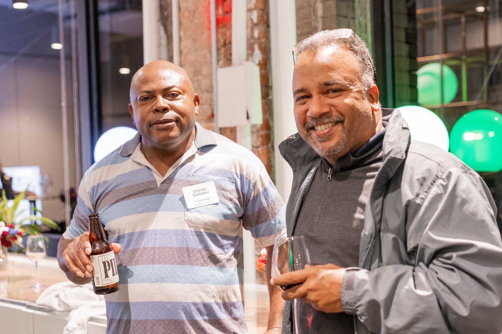 Two men are standing next to each other and one is holding a bottle of beer.
