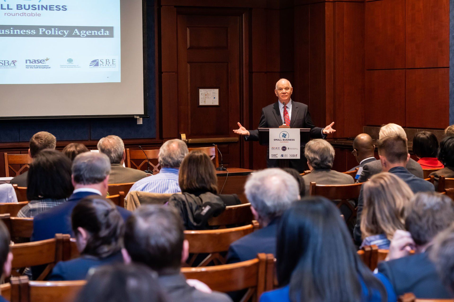 A man is giving a speech to a large group of people in a room.