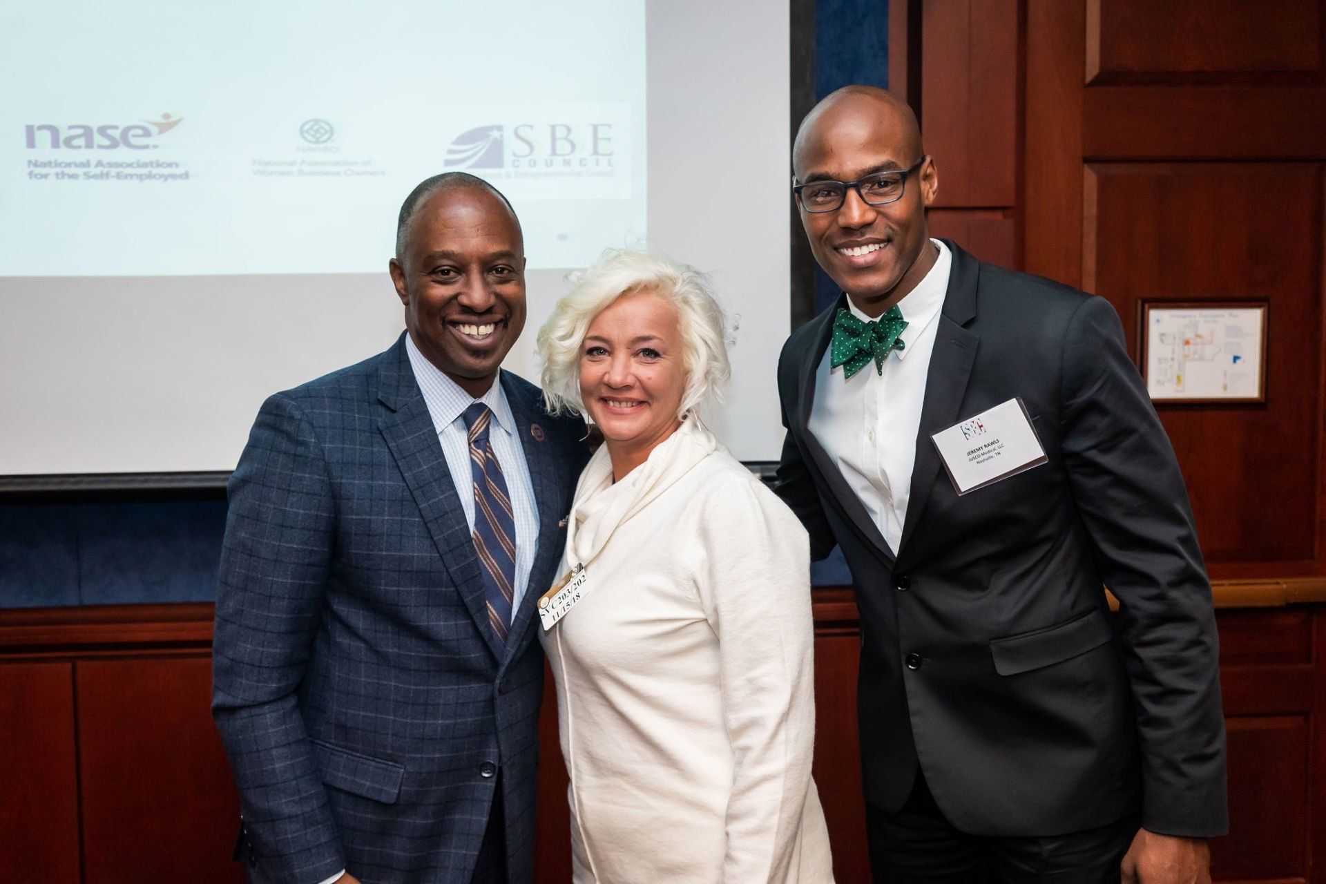 Three people are posing for a picture in front of a projector screen.