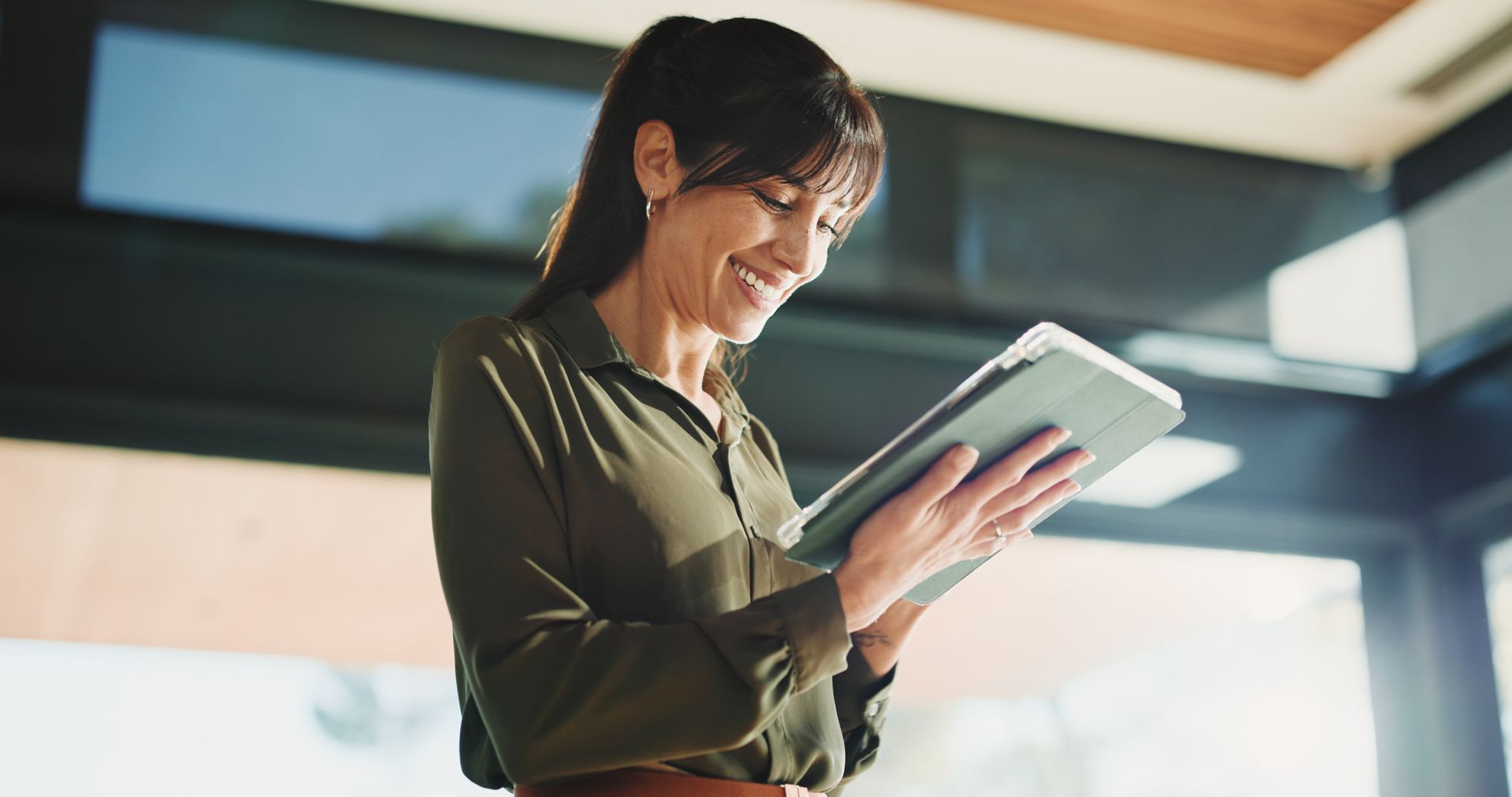 Professional smiling while using property management software on a tablet in a modern office. Professional smiling while using property management software on a tablet in a modern office.