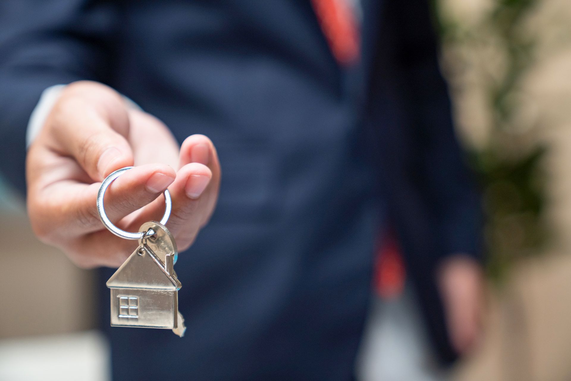 Close-up of a realtor’s hand as he holds a pair of house keys, with a blurry background.