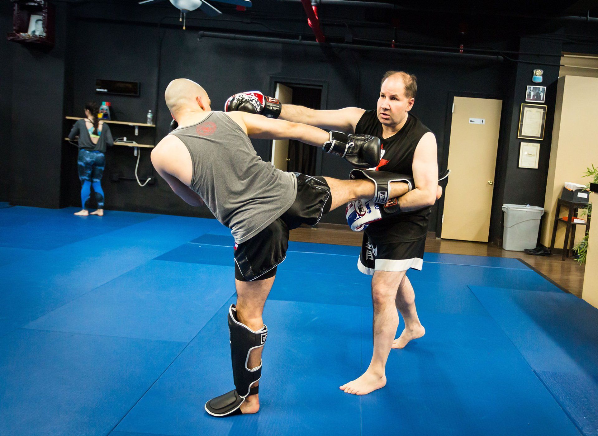Two men are practicing martial arts on a blue mat in a gym.