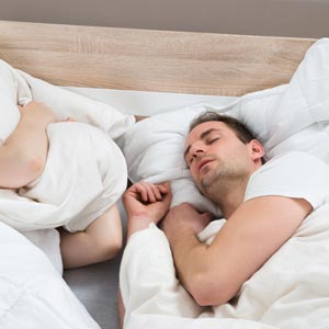 A photo of a man sleeping and snoring and a lady covering her head a pillow to drown out the noise