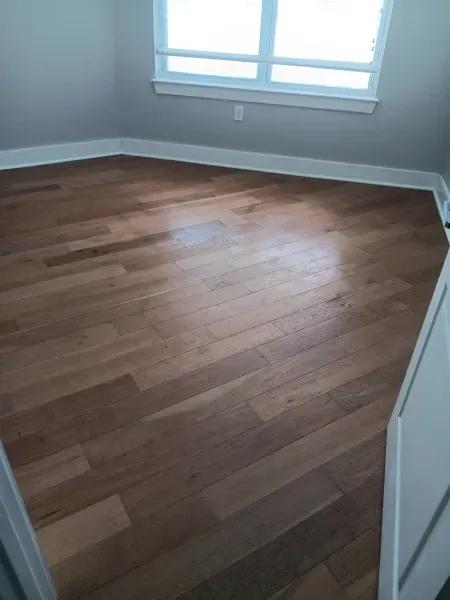 Empty room with hardwood floor, white walls, and a window letting in daylight.