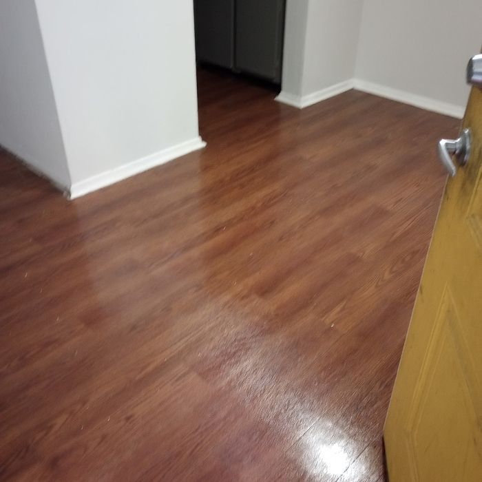 Wood-look laminate floor in a hallway with white walls and an open doorway.