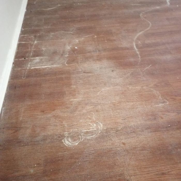 Brown wooden floor with visible scratches and scuff marks, viewed from above.