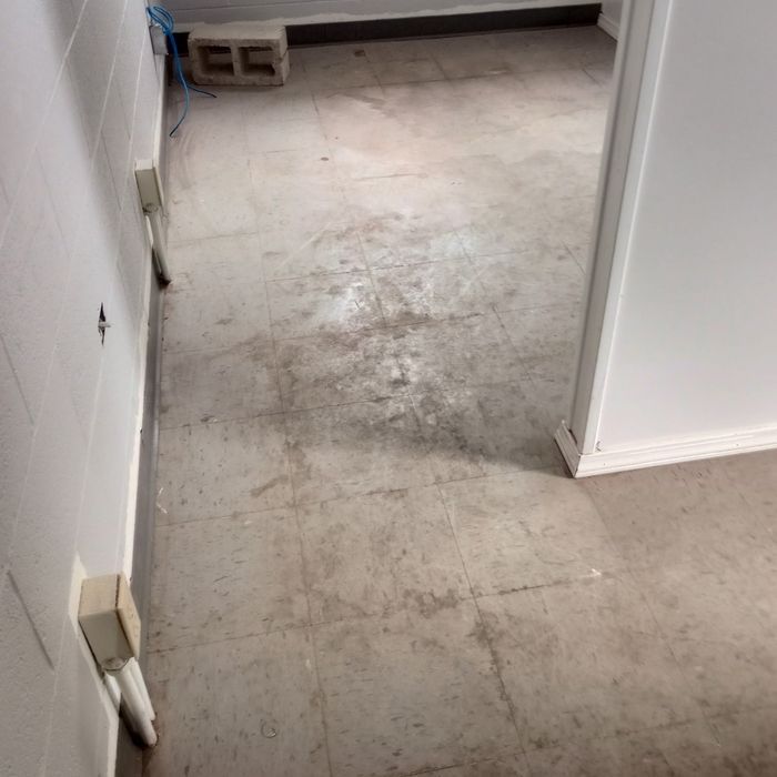 Empty hallway with worn concrete floor, white walls, and a small vent near the far end.