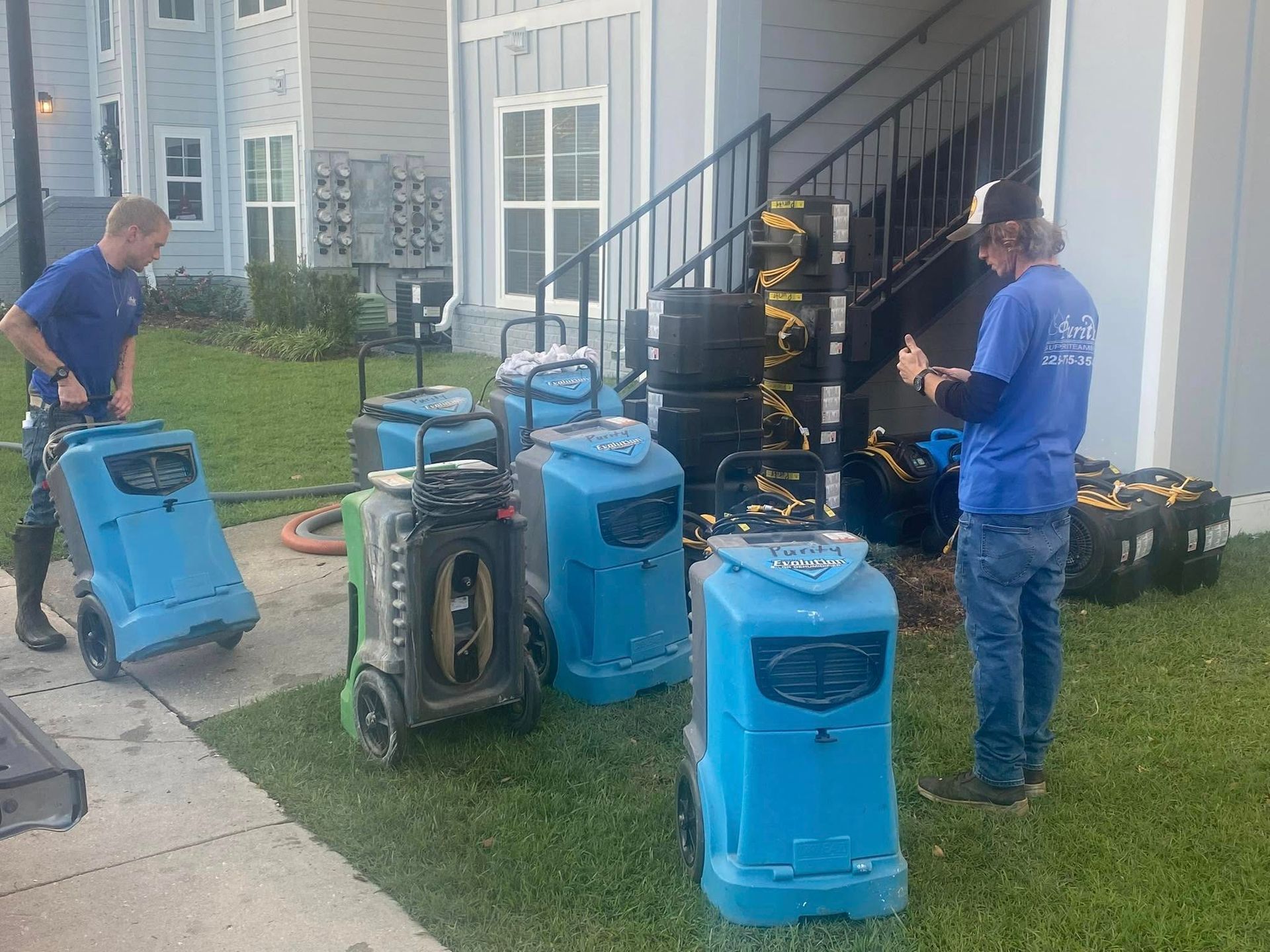 People with blue cleaning machines and hoses working outside a house on the porch and lawn