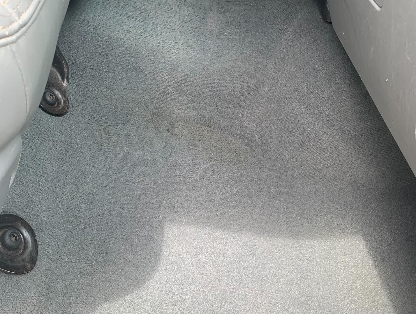 Gray carpeted floor between two light-colored seats with sunlight falling across it