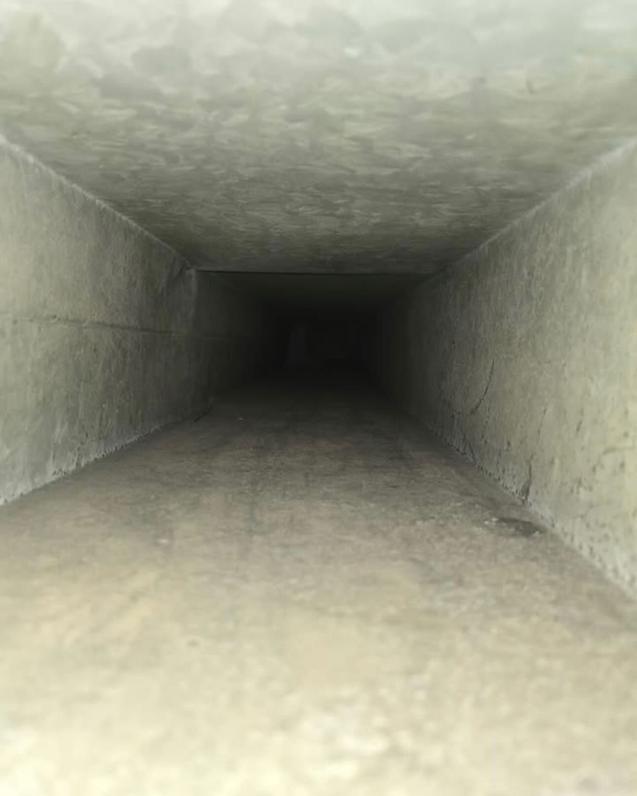 Concrete rectangular ventilation duct, light gray walls fading into darkness