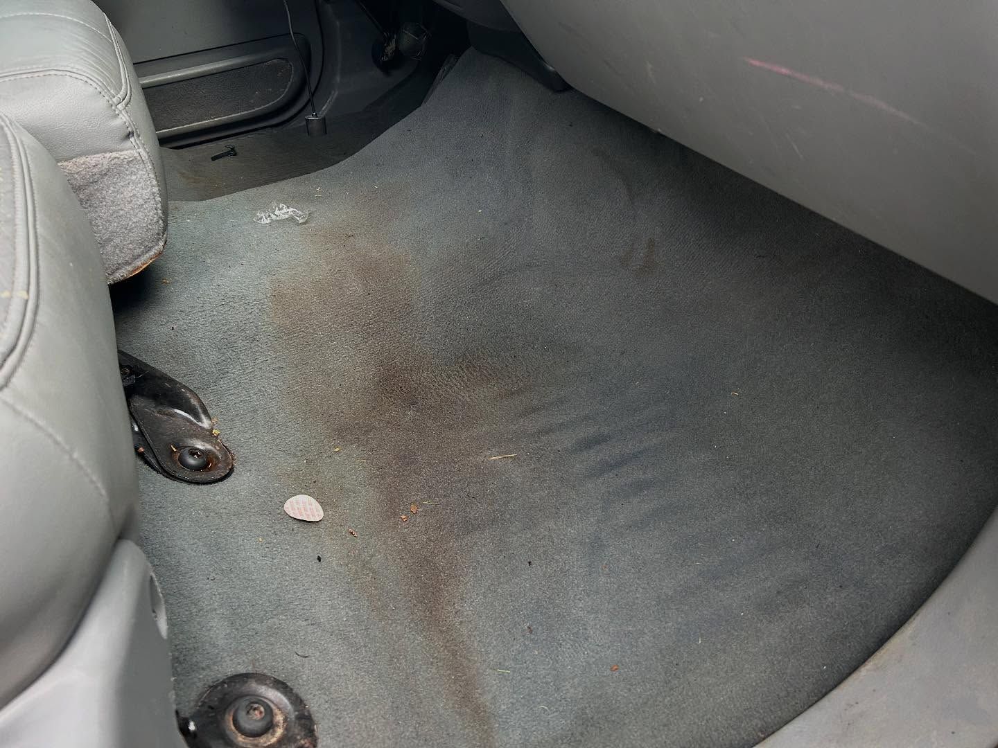 Car floor mat with a large brown stain and a small white object near the seat base