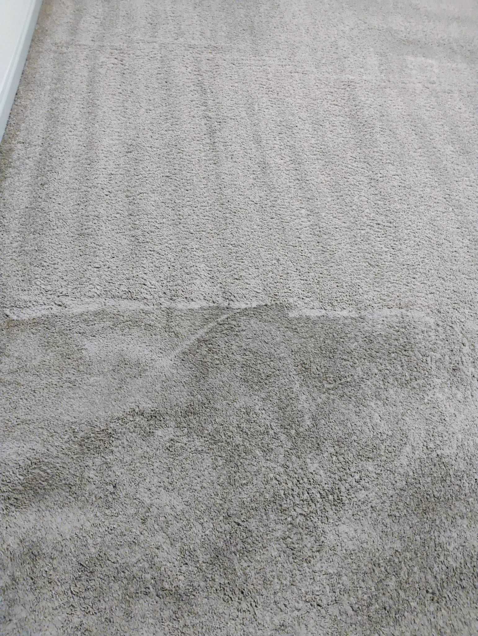 Close-up of a light gray textured carpet with a darker stained patch near the center
