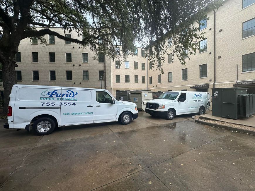 Two white work vans parked in a muddy lot beside beige apartment buildings