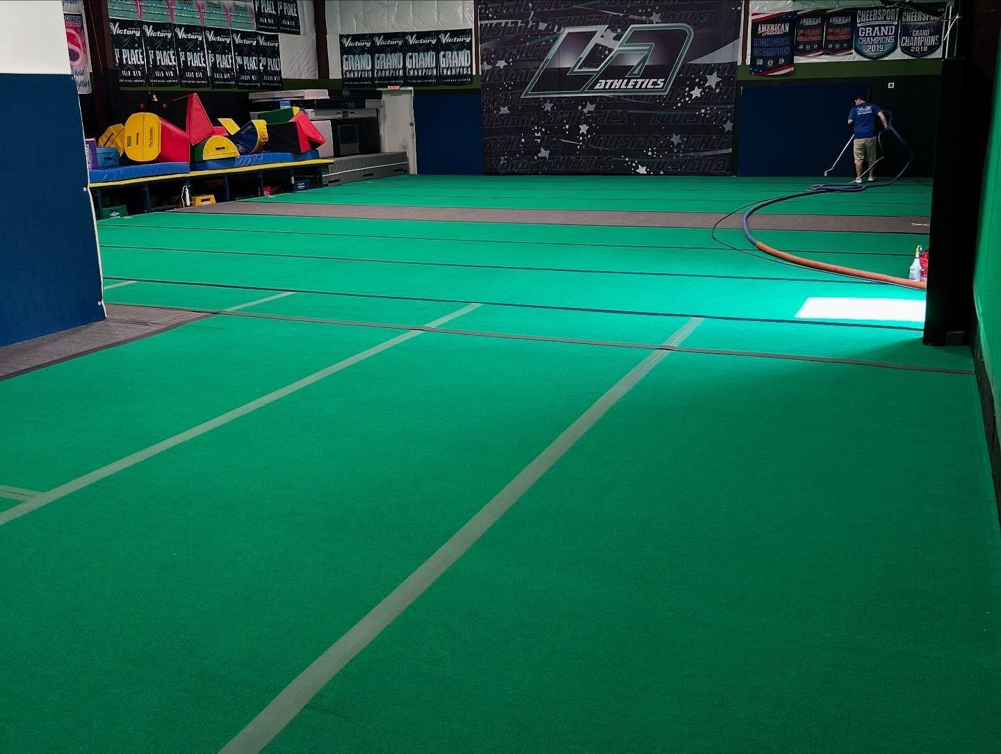 Indoor sports court with green turf, wall banners, and a few people seated at the far left.