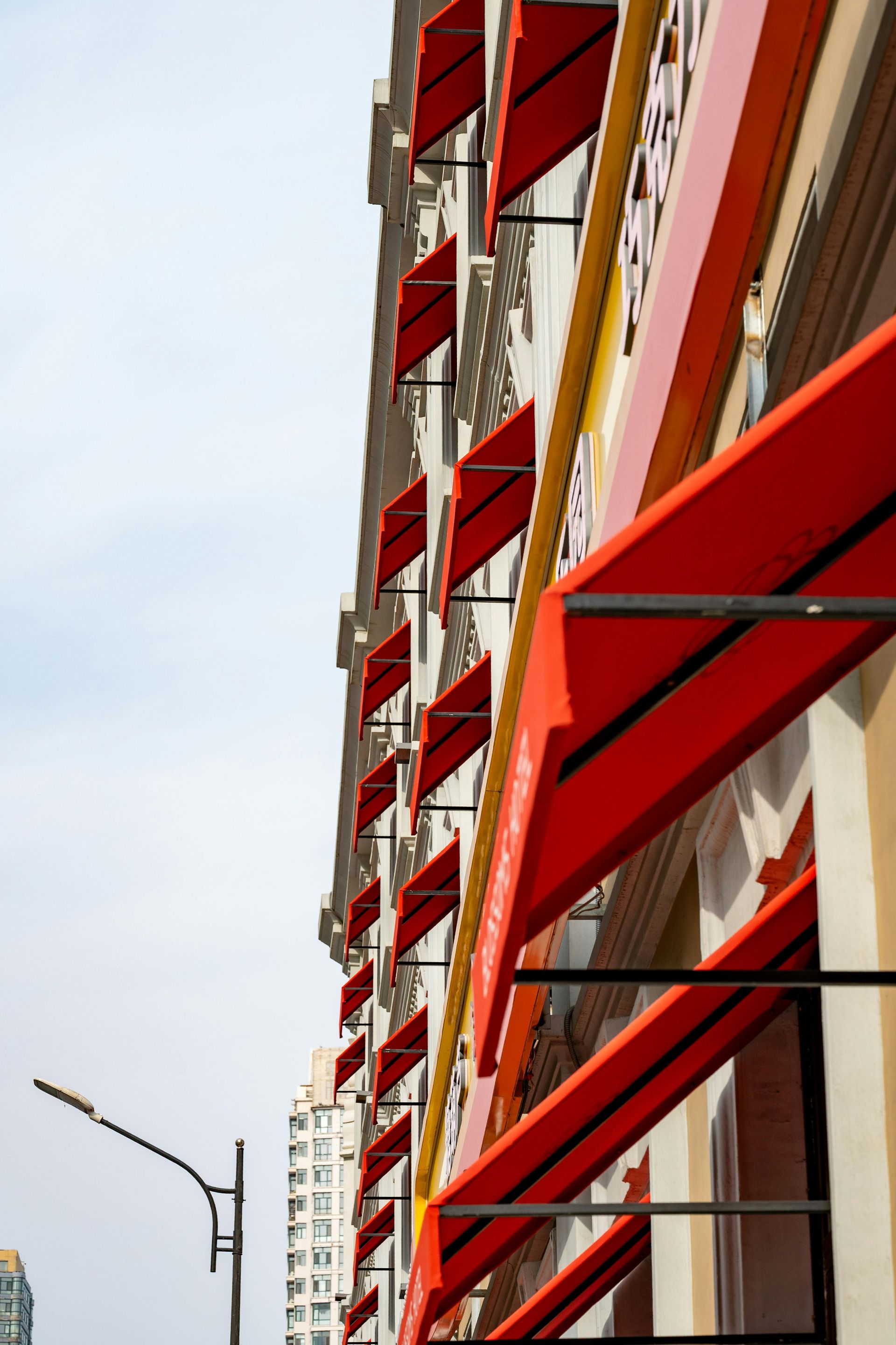 A vertical perspective shows a row of bright red fabric window awnings lining a beige building against a pale sky.