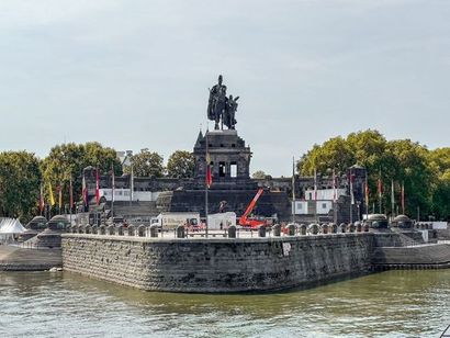 Stone monument on a riverside fort with flags and trees, viewed across the water