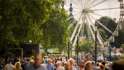 Crowded park fair with a large Ferris wheel and trees in the background