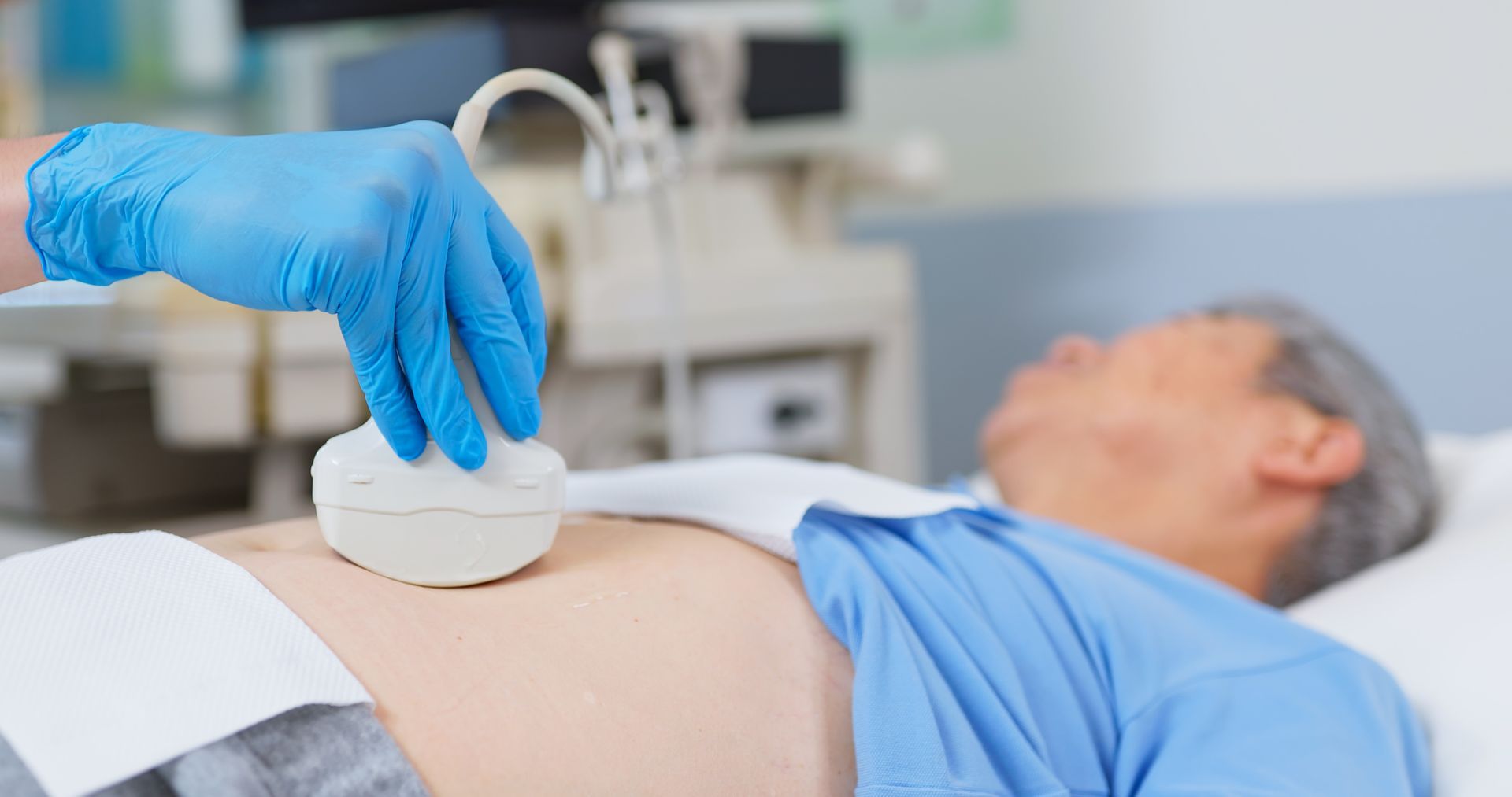 Una persona sottoposta a ecografia addominale. Una mano guantata tiene il trasduttore sullo stomaco.
