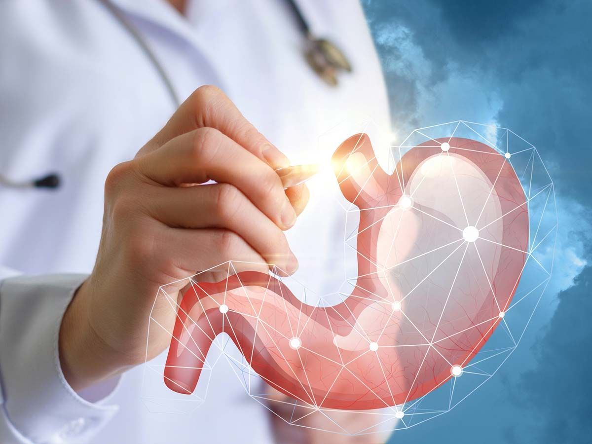 Il medico indica uno stomaco digitalmente rappresentato con nodi di collegamento, su sfondo blu.